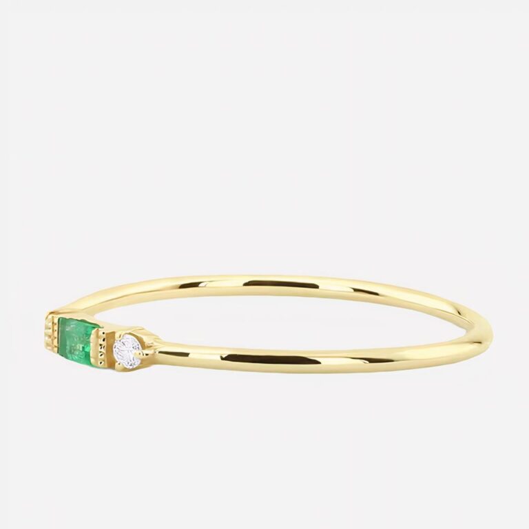 Bague fine dorée avec une pierre verte sur fond blanc.