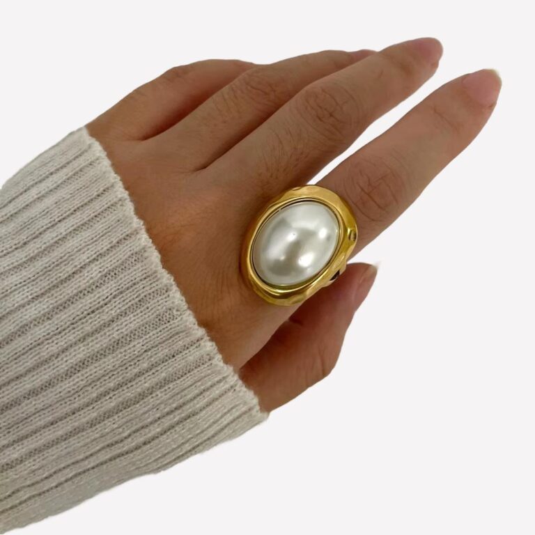 Main qui porte une bague dorée avec une perle nacrée blanche centrale, style classique et taille XXL
