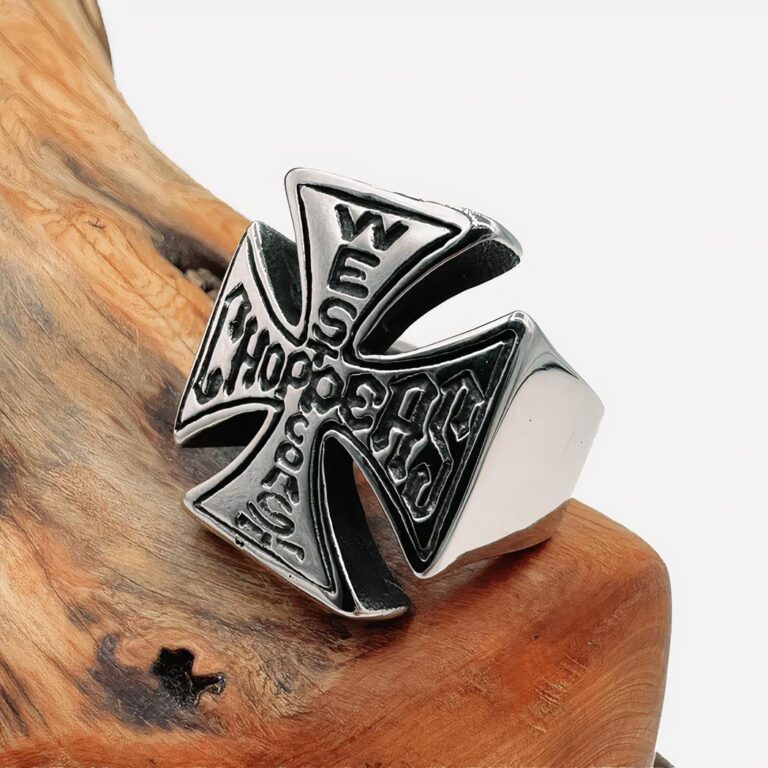 Photo d'une grosse bague pour homme en forme de croix avec inscription gravée posée sur un morceau de bois et un fond gris