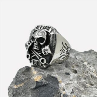 Photo d'une bague chevalière argentée à tête de mort en relief sur une pierre grise, le tout sur fond blanc