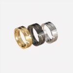 Photo de trois bagues anneaux double pour homme, une dorée, une noire et une argentée présentées sur un morceau de pierre beige