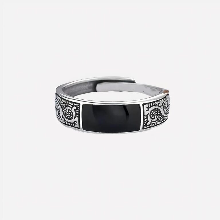 Bague réglable motifs dragon Photo d'une bague réglable pour homme en acier à motifs dragon sur le tour et pierre noire rectangulaire, posée sur un papier blanc avec au fond de l'image une rose des sables