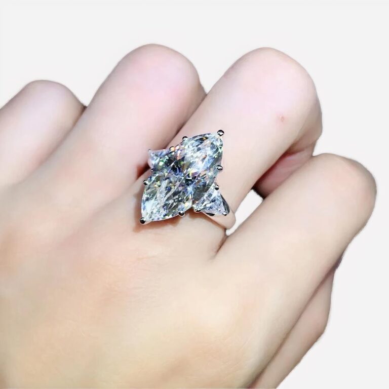 Photo d'une main de femme portant une bague marquise en argent et moissanite sur un fond gris et bleu