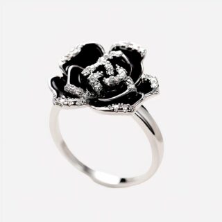 Photo d'une bague index femme argentée ornée d'un camélia noir et de zirconiums sur un fond très clair et blanc