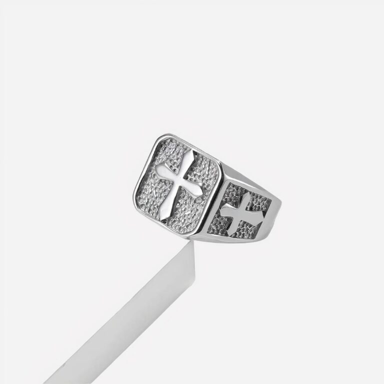 Bague homme chevalière croix Photo d'une bague argentée pour petit doigt homme, chevalière ornée de croix en relief, le tout sur un fond blanc et gris clair