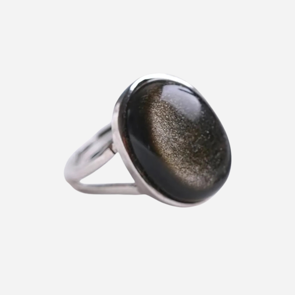 Bague ajustable en argent et obsidienne dorée sur fond gris très clair.
